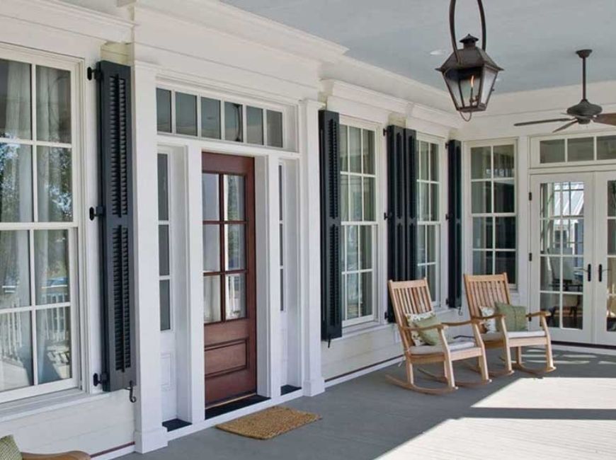 front porch with windows with black shutters and two chairs